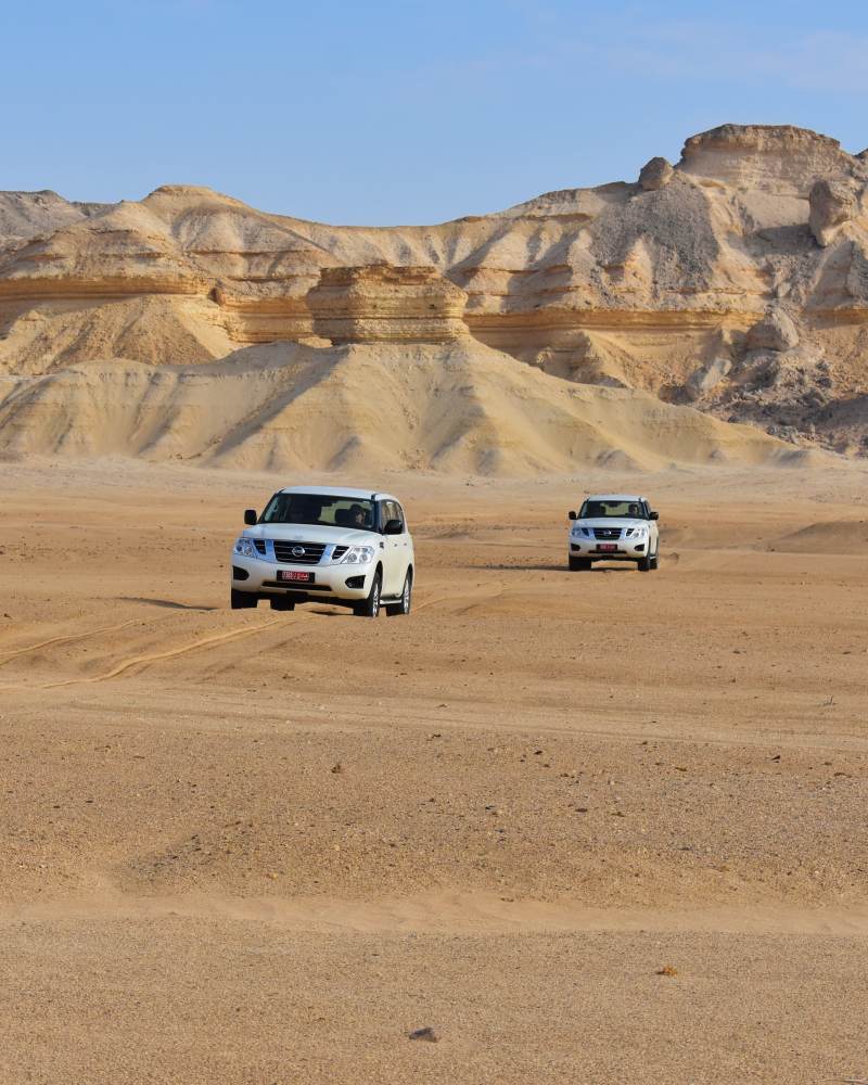 Two Nissan Patrols (Y62) driving with the Al Huqf Escarpment behind them, Oman