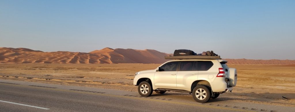 A Toyota Prado parked at the side of the Rub al Khali Road with tall sand dunes in the distance