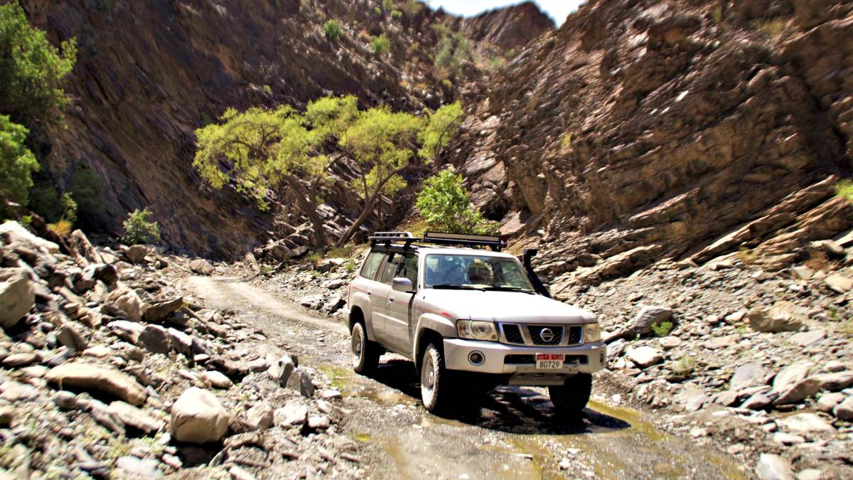 A Nissan Patrol drives along a narrow track through the hills of Wadi Bani Auf