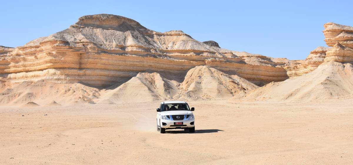 A Nissan Patrol drives on the desert beside the layered escarpment of the Al Huqf area in Oman