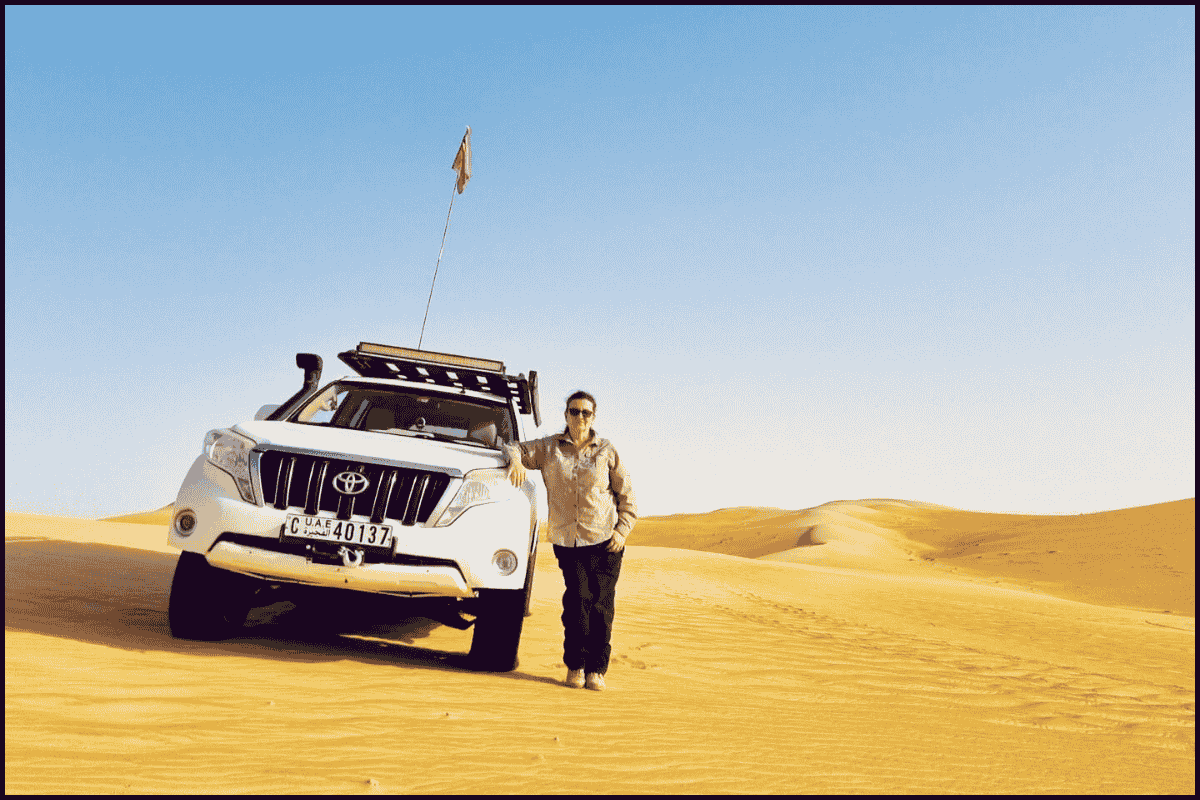 4x4 vehicle and traveller standing in a sandy UAE desert.