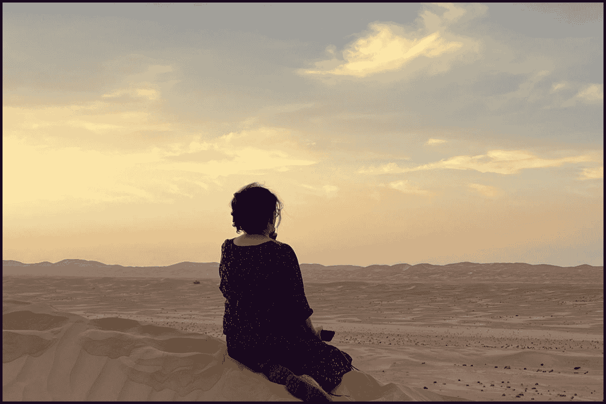 Woman sitting on sand dune watching sunset in the UAE desert.