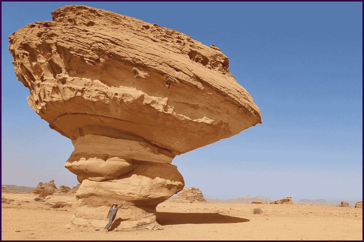 Traveller posing beside giant mushroom-shaped sandstone rock in Saudi Arabia.