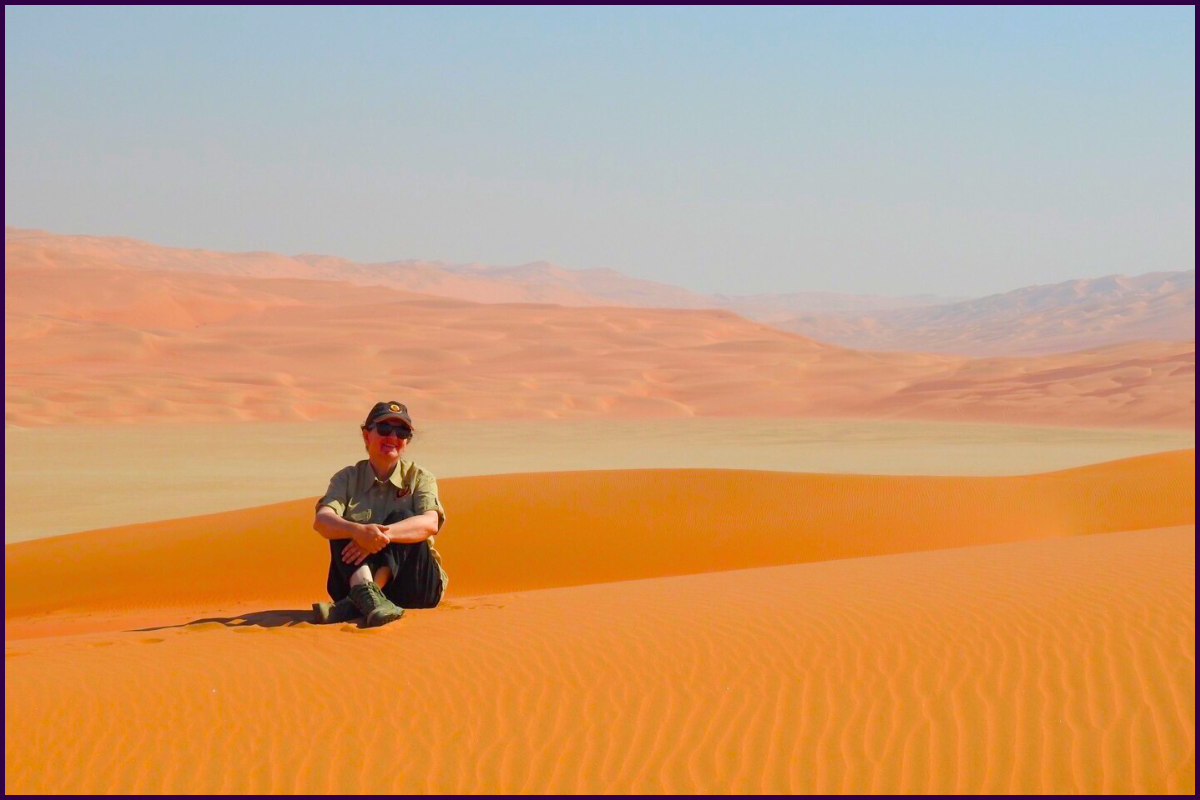 Female Traveller sitting atop a sand dune overlooking the desert landscape.